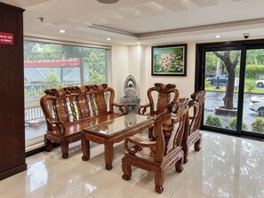 A conference room with a large table and ornate wooden chairs, a painting on the wall, and a view of the outside through large windows. - Lychee Hotel (Da Nang)
