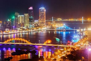 Paisaje urbano nocturno con edificios iluminados, un puente y un río.