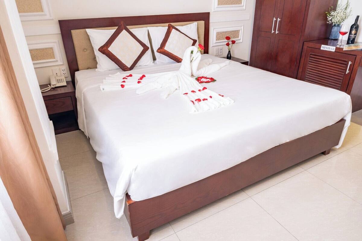 A neatly made bed with a white bedspread, a wooden headboard, and decorative pillows.