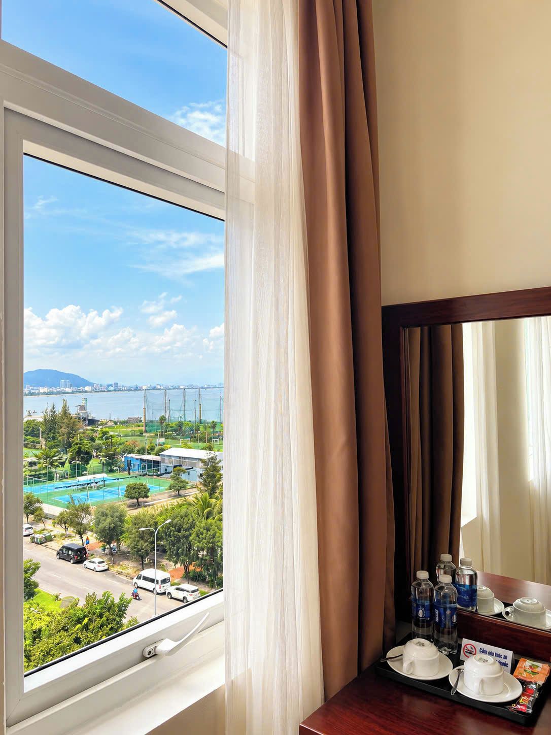 Une chambre d’hôtel dotée d’une grande fenêtre donnant sur une piscine et sur le paysage urbain.