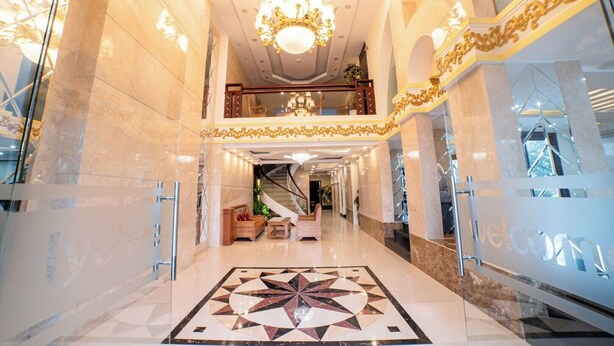 A grand lobby with a geometric floor design, a chandelier, and a staircase leading to an upper level. - Lychee Hotel (Da Nang)