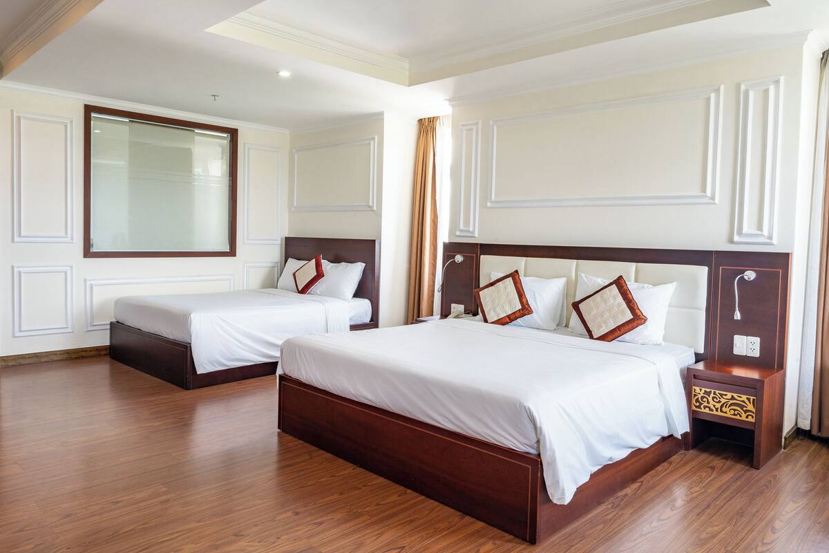 A hotel room with two beds, wooden flooring, and a large mirror on the wall.
