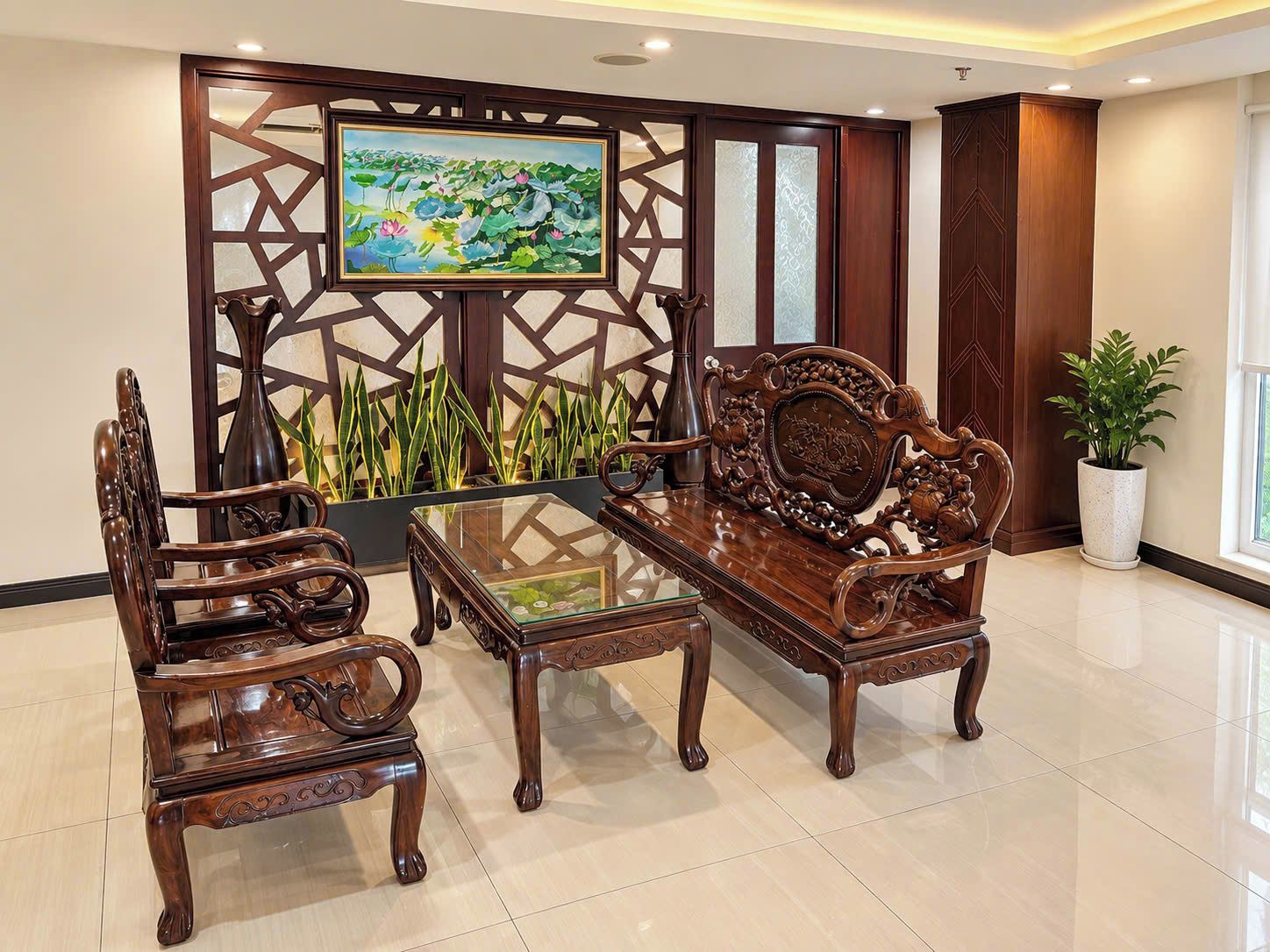 A traditional wooden sofa and chairs set around a glass-top coffee table in a well-lit room with a decorative screen and a painting.