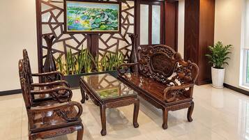 A traditional wooden sofa and chairs set around a glass-top coffee table in a well-lit room with a decorative screen and a painting.