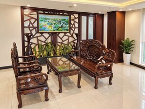 A traditional wooden sofa and chairs set around a glass-top coffee table in a well-lit room with a decorative screen and a painting. - Lychee Hotel (Da Nang)
