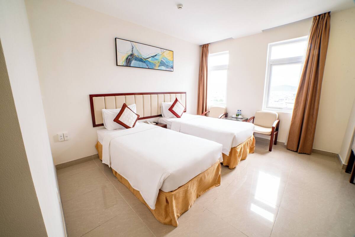 A hotel room with two beds, a desk, a chair, and a window with curtains.
