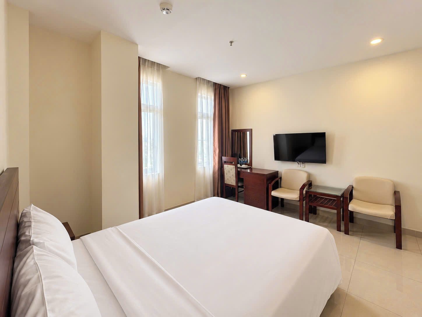 Una habitación de hotel con una cama grande, un escritorio, una silla, un televisor y cortinas.