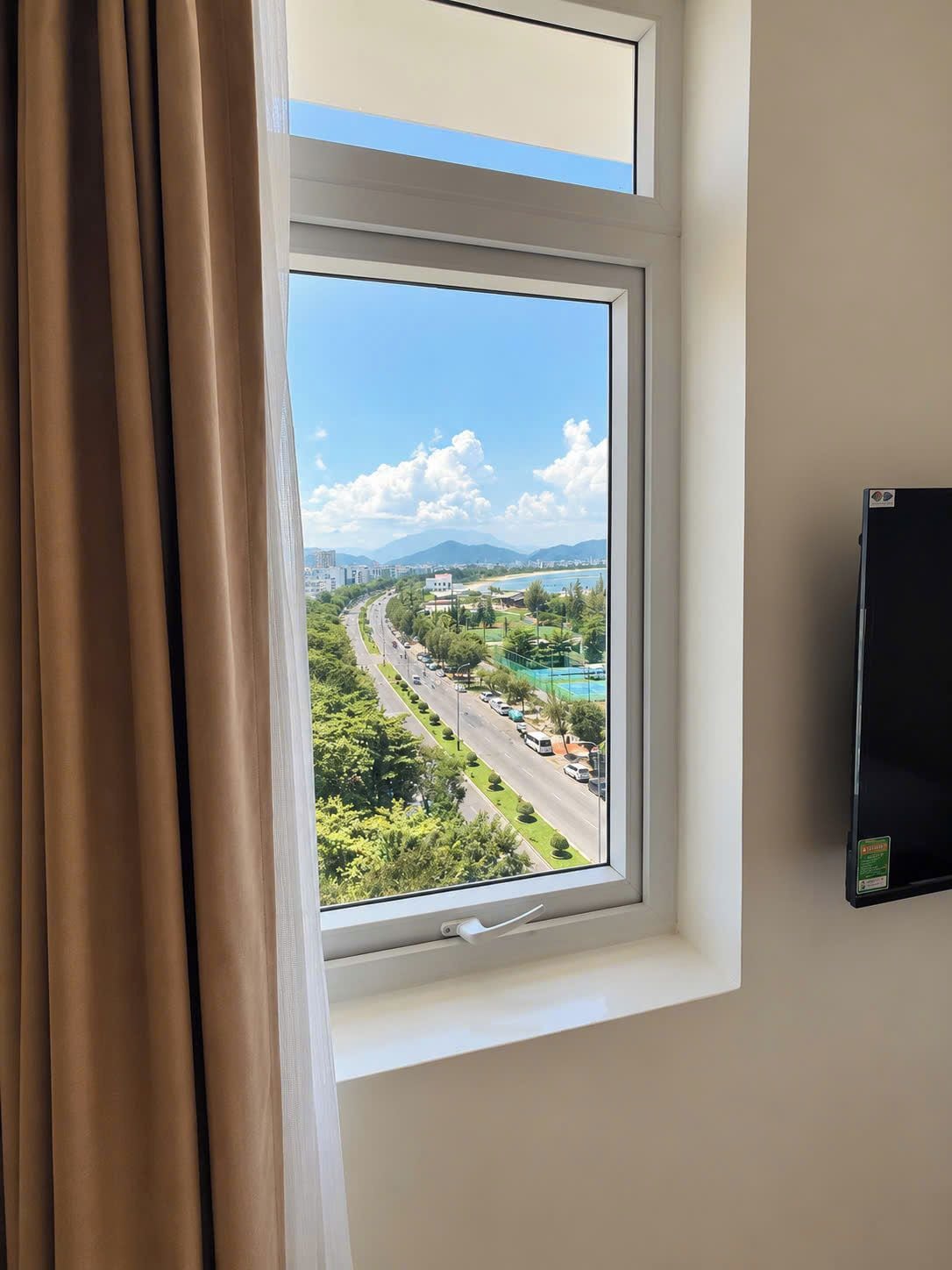 A window with a view of a road, greenery, and distant buildings.