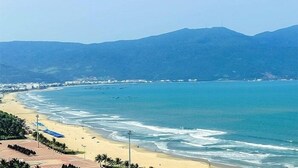 A beach with clear blue waters, a sandy shore, and a mountain in the background. - Lychee Hotel (Da Nang)