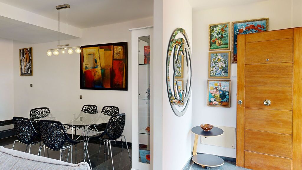 Un comedor moderno con una mesa redonda y sillas, un cuadro abstracto grande y una puerta de madera con obras de arte enmarcadas.
