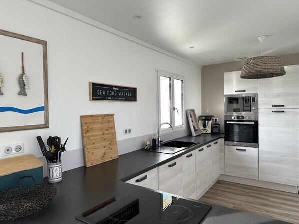 A modern kitchen with a black countertop, stainless steel appliances, and a wooden cutting board.