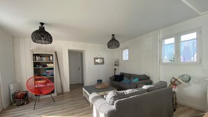 Un amplio salón con un sofá gris, una butaca roja y una estantería.