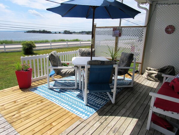 A wooden deck with a table and chairs, a blue umbrella, and a view of the water.