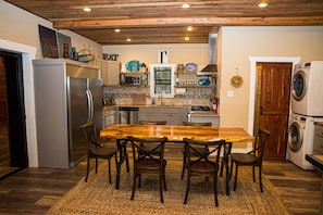 A kitchen with a wooden dining table, chairs, a refrigerator, microwave, sink, and a washing machine.