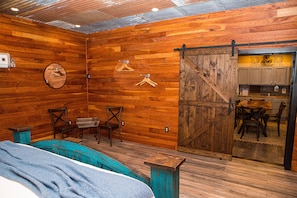 Cozy room with a large barn-style door leading to a kitchen area, featuring a comfortable bed and seating for two.
