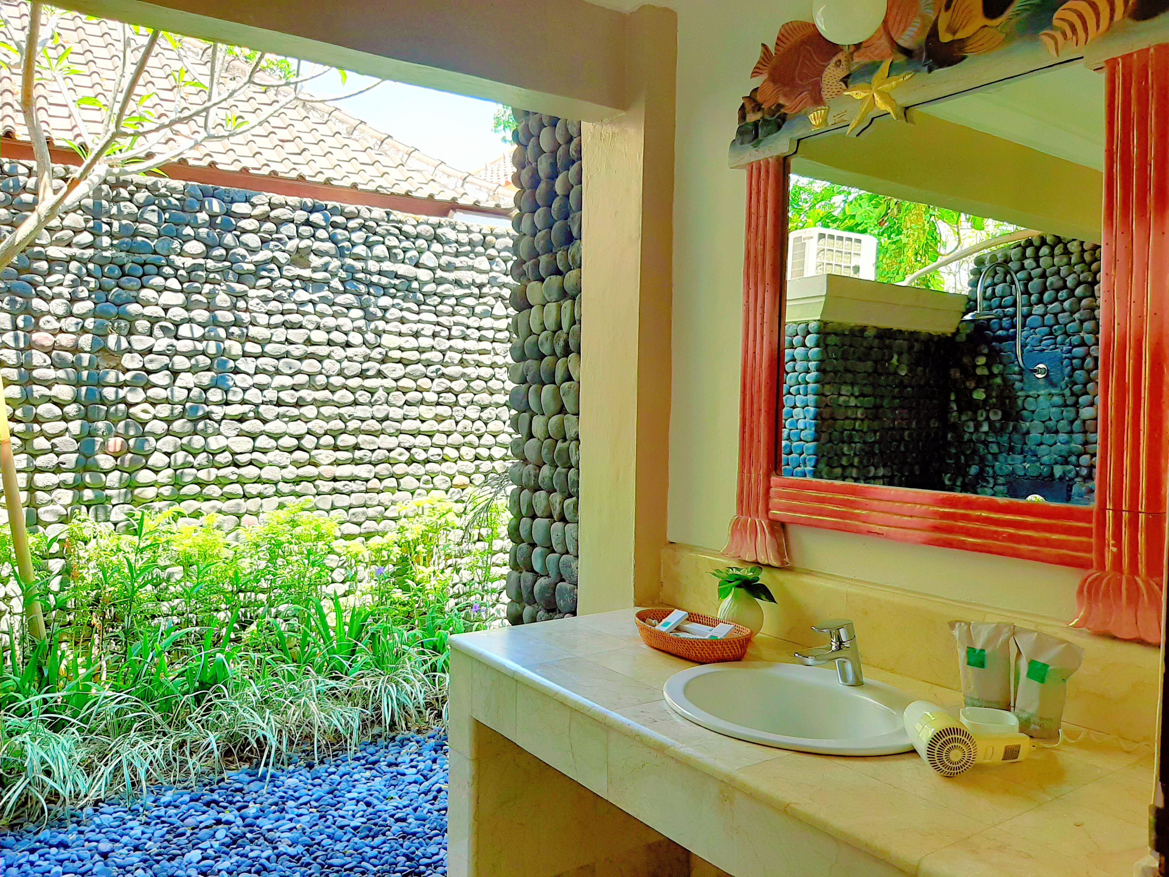 A bathroom with a stone wall, a sink, a mirror, and a window with a view of greenery.