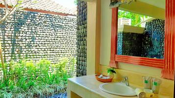 A bathroom with a stone wall, a sink, a mirror, and a window with a view of greenery.