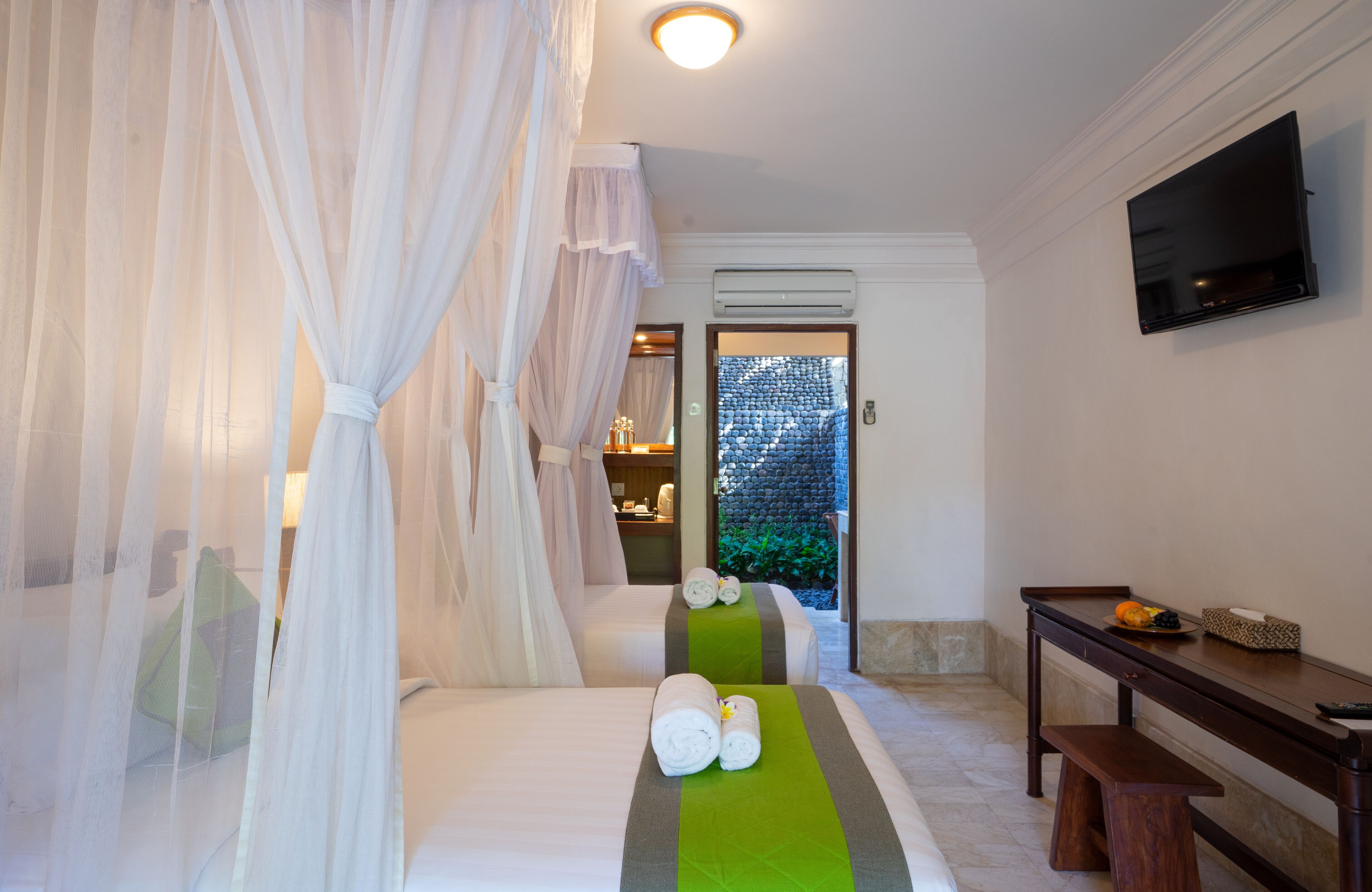A hotel room with two beds, a TV, a desk, and a view of the outdoors.