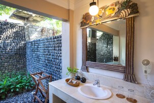 Un baño con pared de piedra, una silla de madera, un lavabo y un espejo.