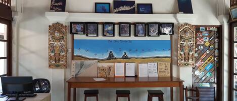 A room with a wooden desk, two stools, a computer, and a wall decorated with framed pictures and a large mural of a beach scene.