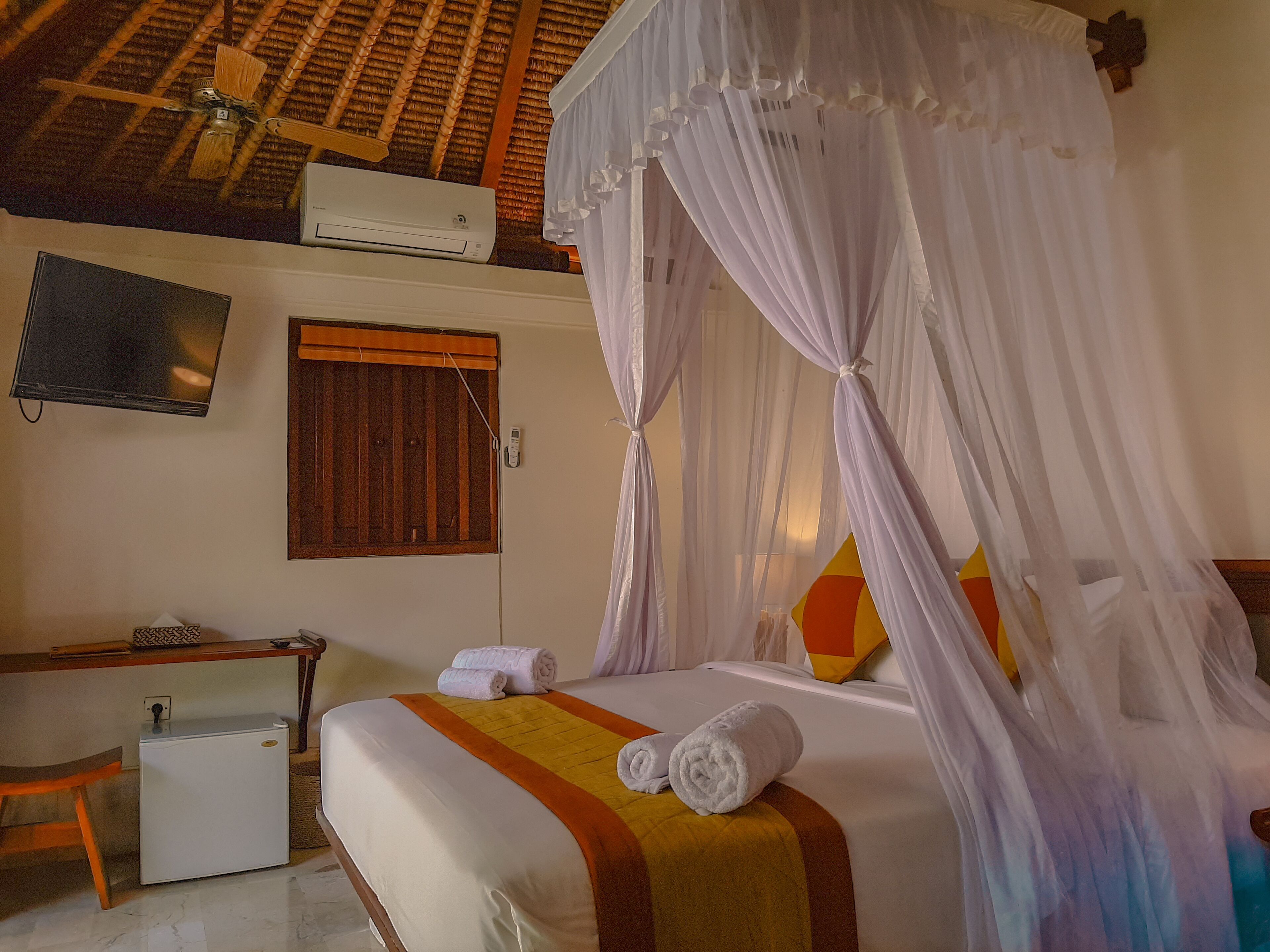 A hotel room with a bed, a TV, a desk, and a refrigerator.