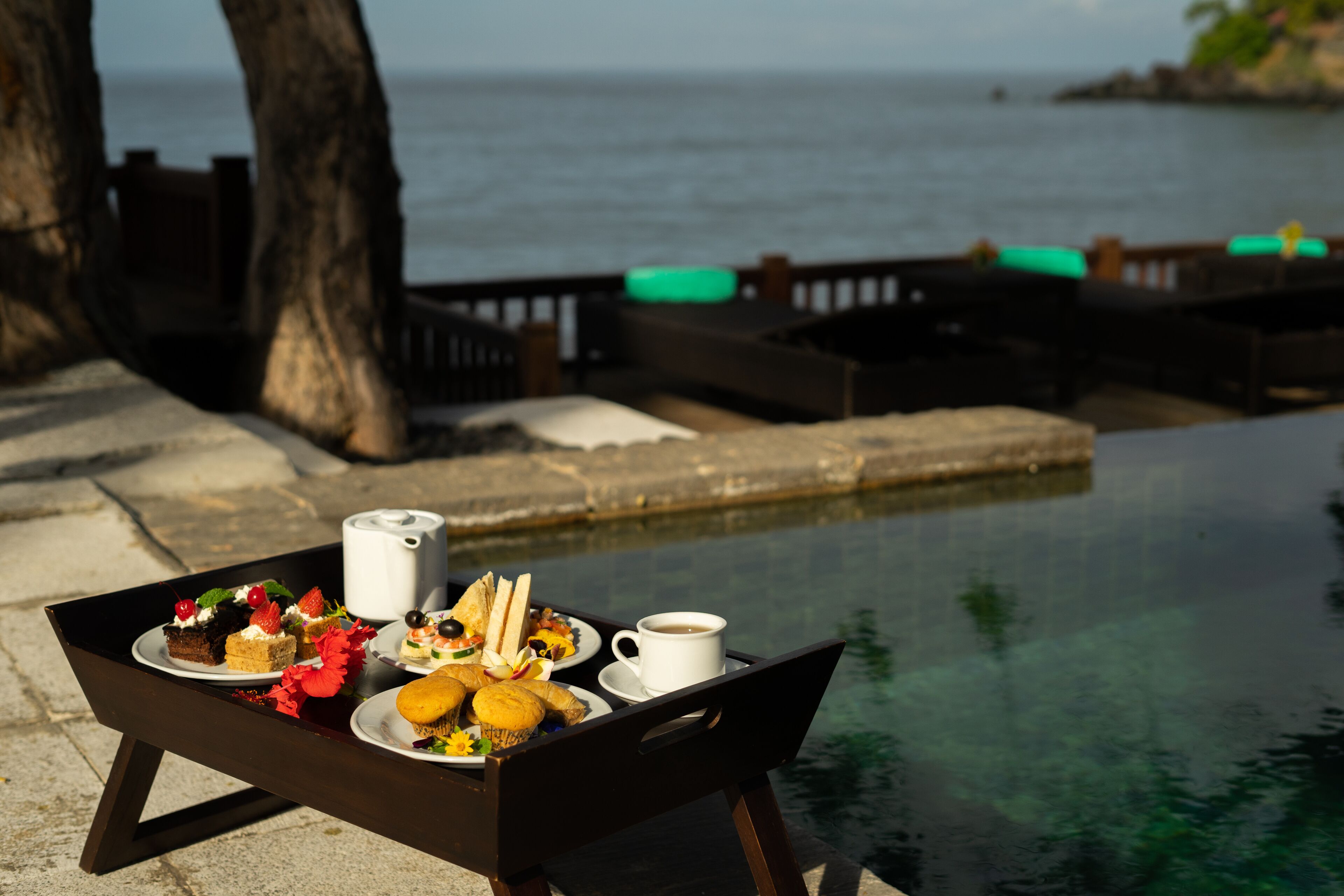 A tray with food and a cup by a poolside with a view of the sea.