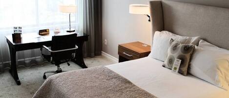 A hotel room with a large bed, a desk with a chair, a nightstand, and a window with curtains.