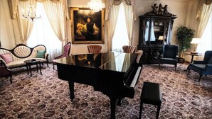 A grand room with a black grand piano, a large painting, a chandelier, and classic furniture. - Executive Queen Room in Minneapolis Boutique Hotel (Minneapolis)