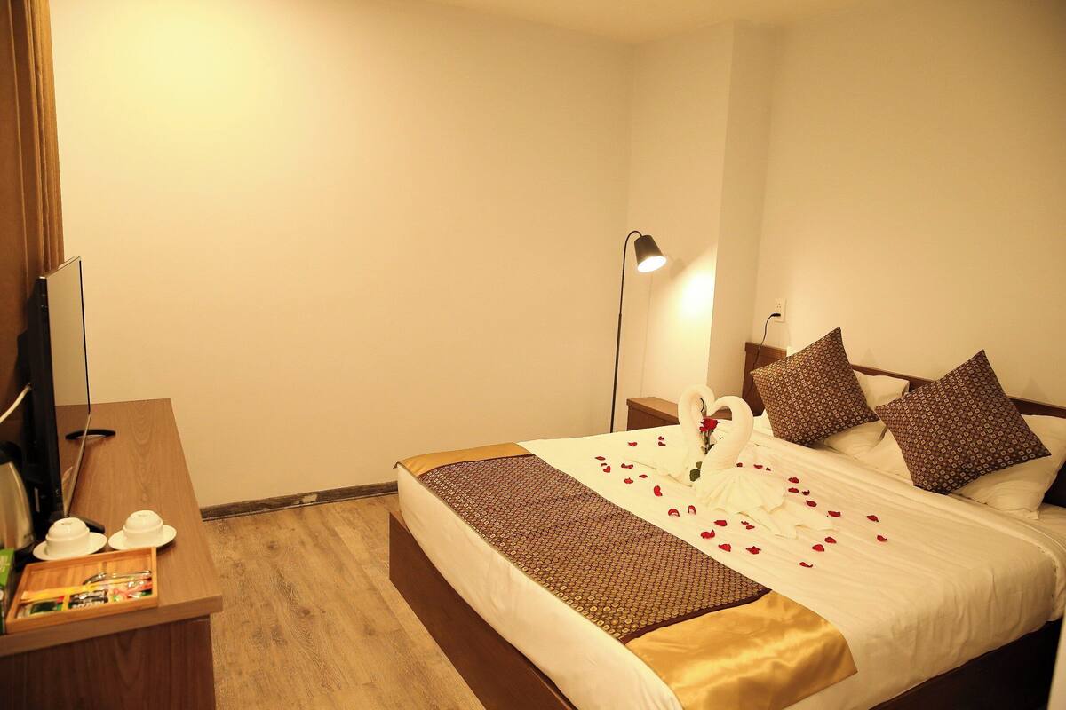 Et hotelværelse med en pænt redt seng, et skrivebord med lampe og en kommode.