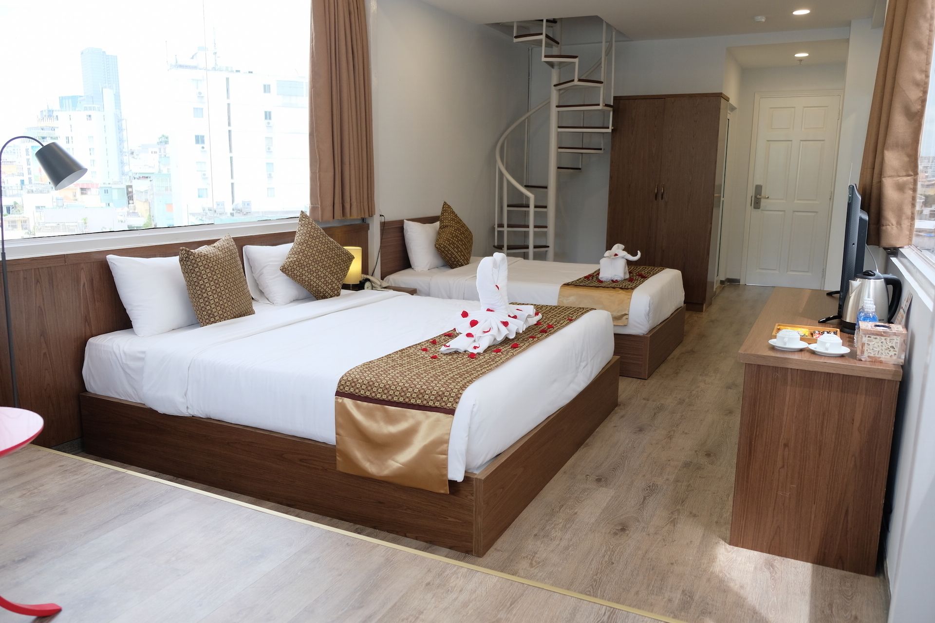 Une chambre d’hôtel avec deux lits, un bureau, une chaise, un escalier et une vue sur la ville.
