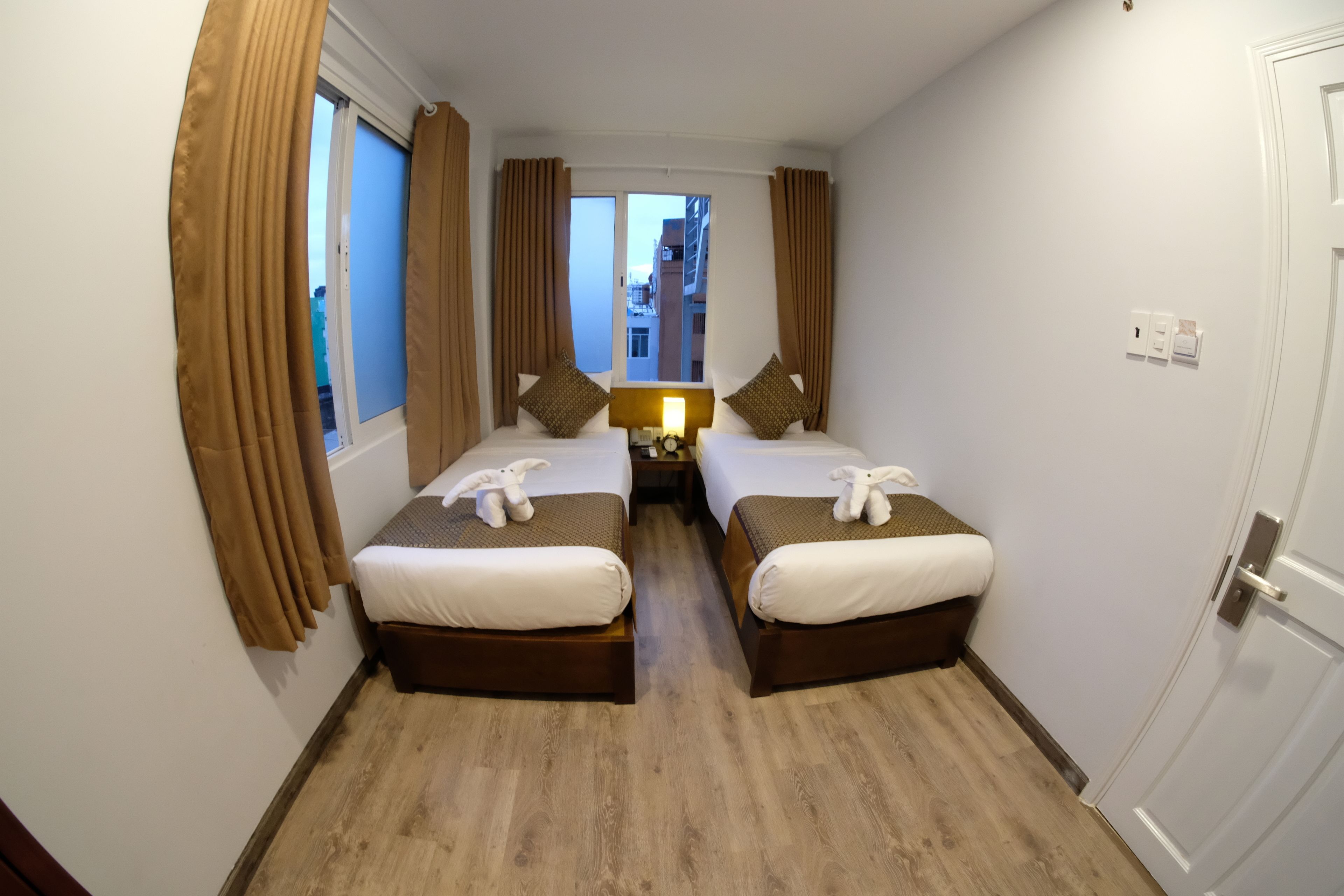 Habitación de hotel con dos camas, cabeceros marrones, ropa de cama blanca y vistas a la ciudad.