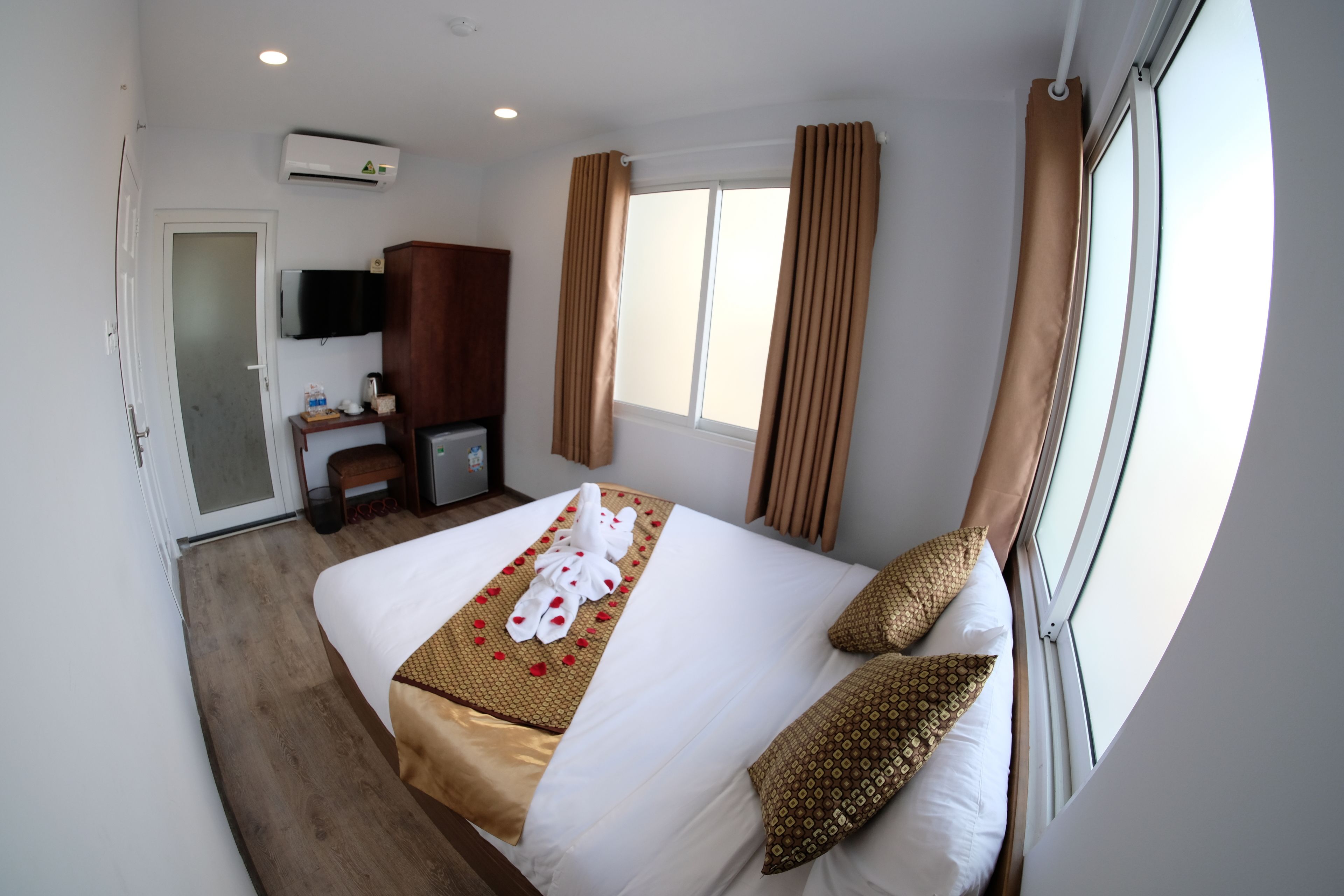 A hotel room with a bed, a TV, an air conditioner, a desk, and a window with curtains.