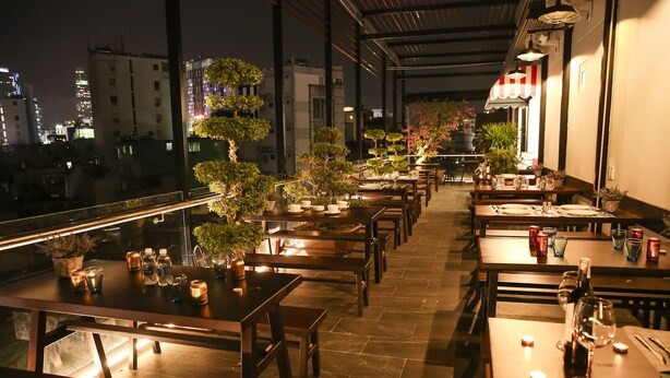 A rooftop restaurant with multiple tables and chairs, potted plants, and a view of the cityscape at night. - The Umi Hotel (Ho Chi Minh City)