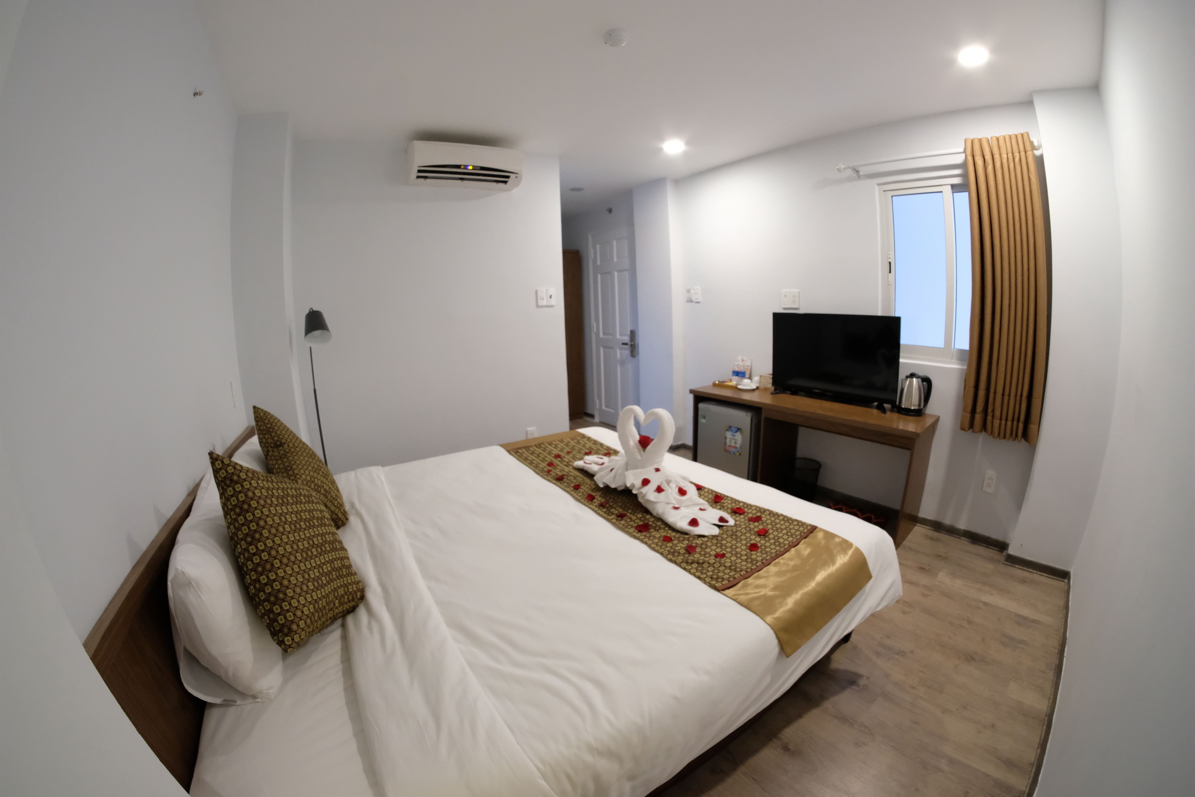 Una habitación de hotel con cama, escritorio, televisión y ventana con cortinas.