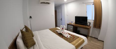Una habitación de hotel con cama, escritorio, televisión y ventana con cortinas.