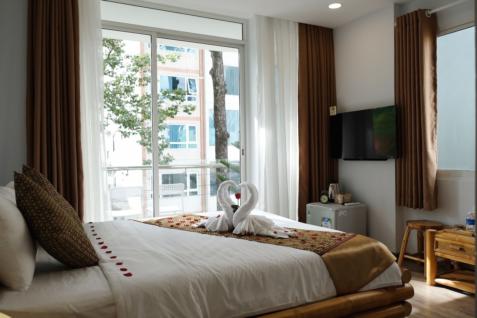 Ein Hotelzimmer mit einem großen Bett, einem Fernseher, einem kleinen Tisch und Blick auf Gebäude und Bäume.