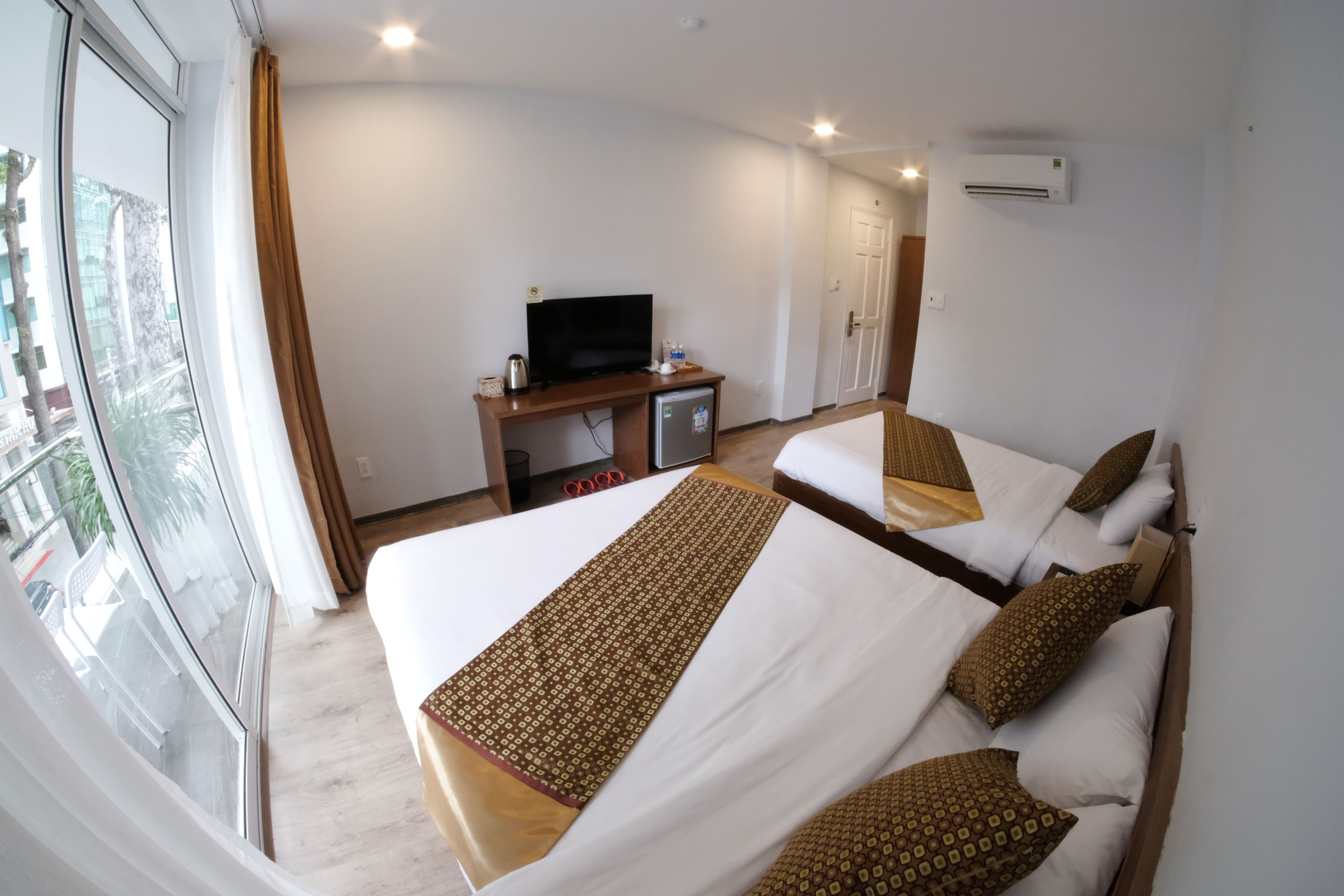 A hotel room with two beds, a TV, a desk, and a window with curtains.