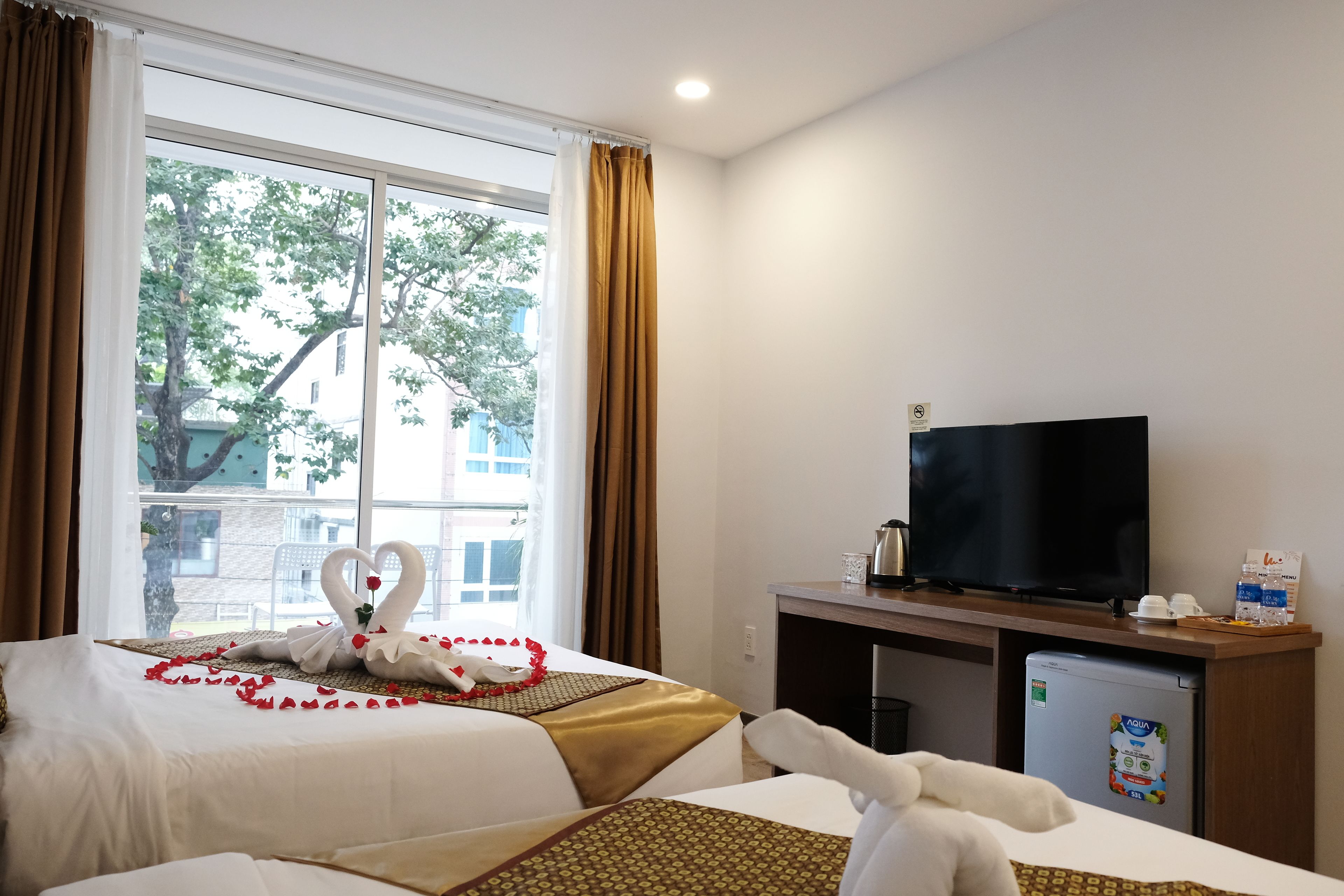 A hotel room with a bed, a TV, a mini-fridge, and a window with curtains.