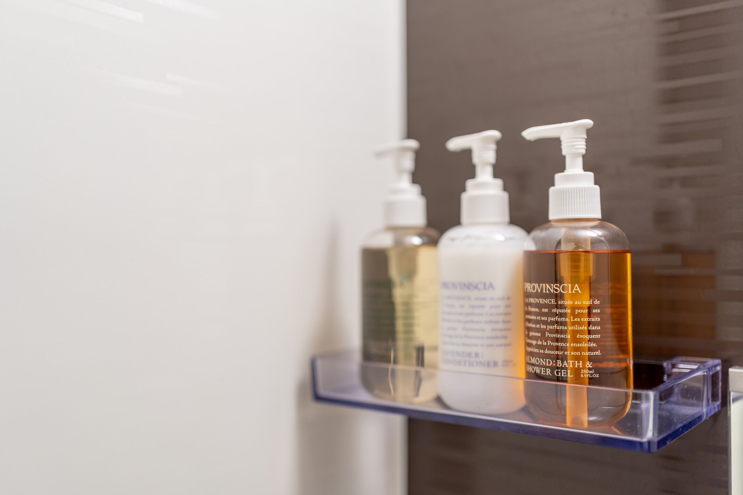 A bathroom shelf with three bottles of shower gel.