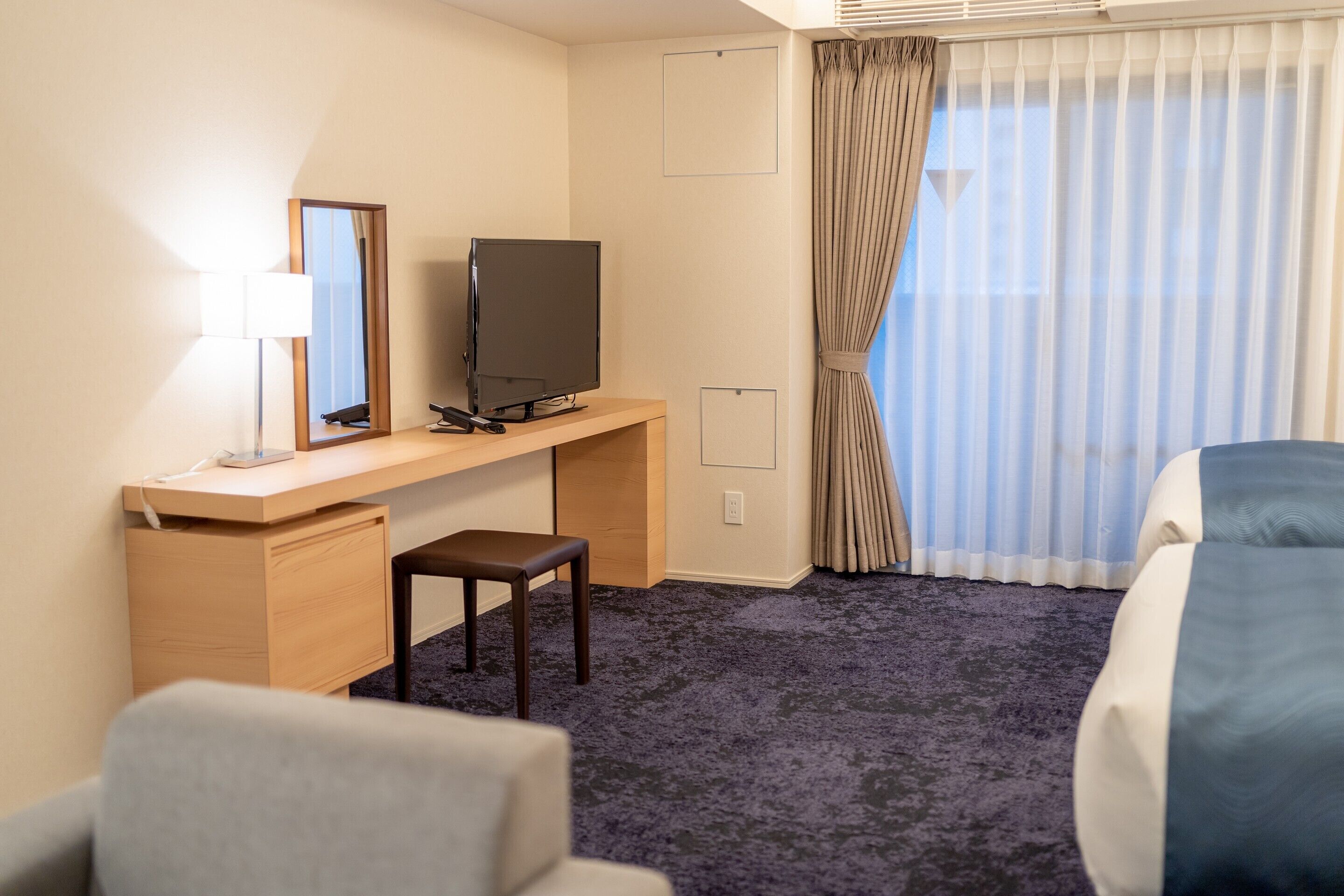 A hotel room with a desk, television, chair, and a bed.