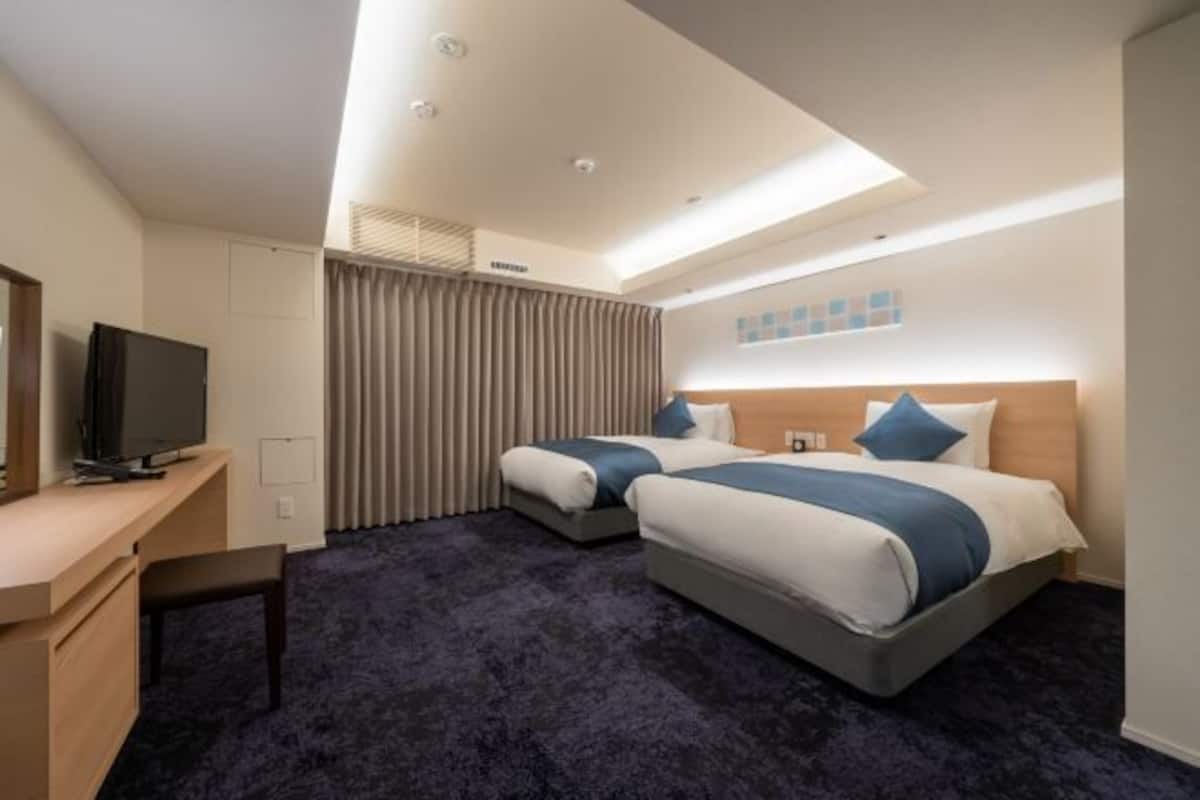 Ett hotellrum med två sängar, ett skrivbord med en tv och en taklampa.