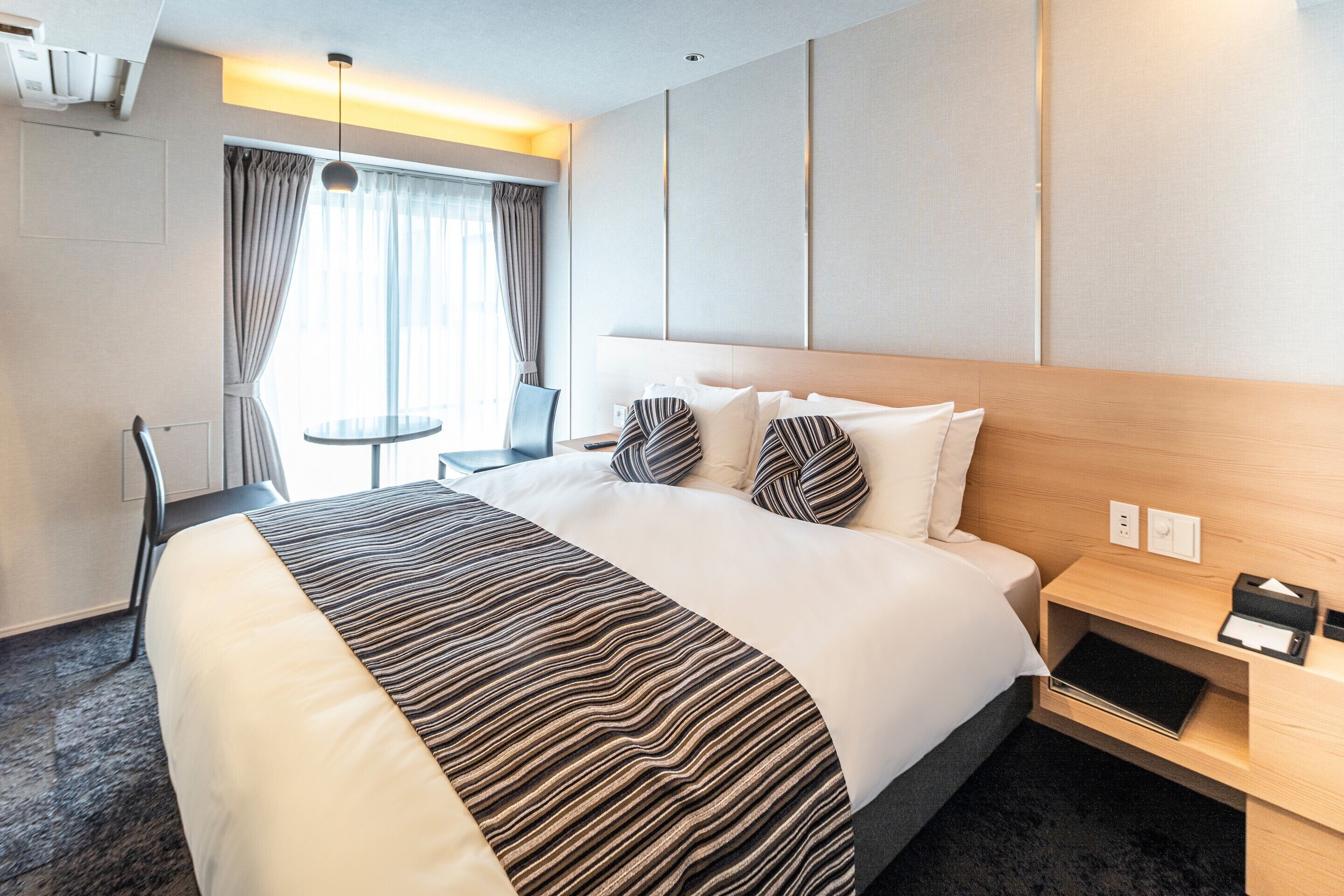 Una habitación de hotel con una cama grande, una mesita de noche, una silla y una pequeña mesa.