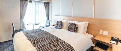 Una habitación de hotel con una cama grande, una mesita de noche, una silla y una pequeña mesa.