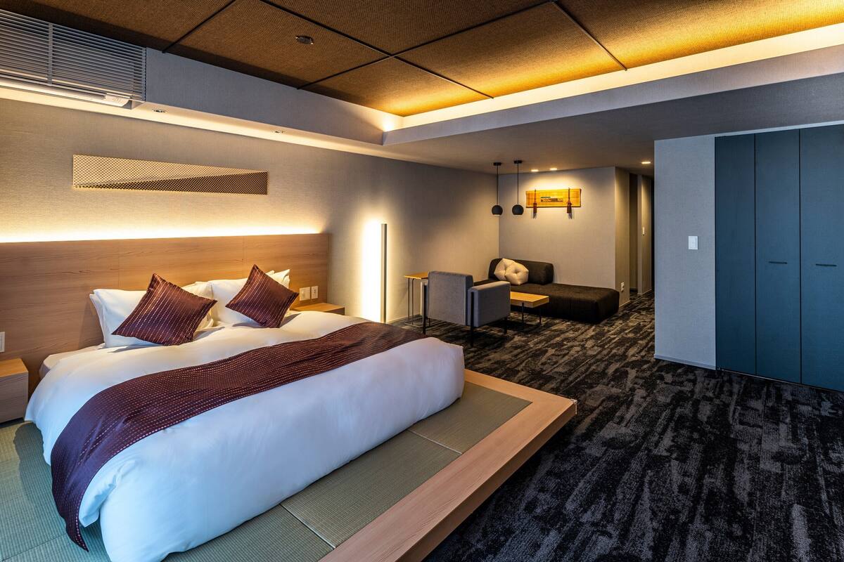 A hotel room with a large bed, a desk, a chair, and a wardrobe.