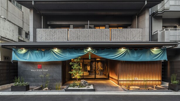 Entrada de un hotel con porche cubierto, un letrero que dice "Mayu Grace Hotel" y un pequeño jardín con plantas.