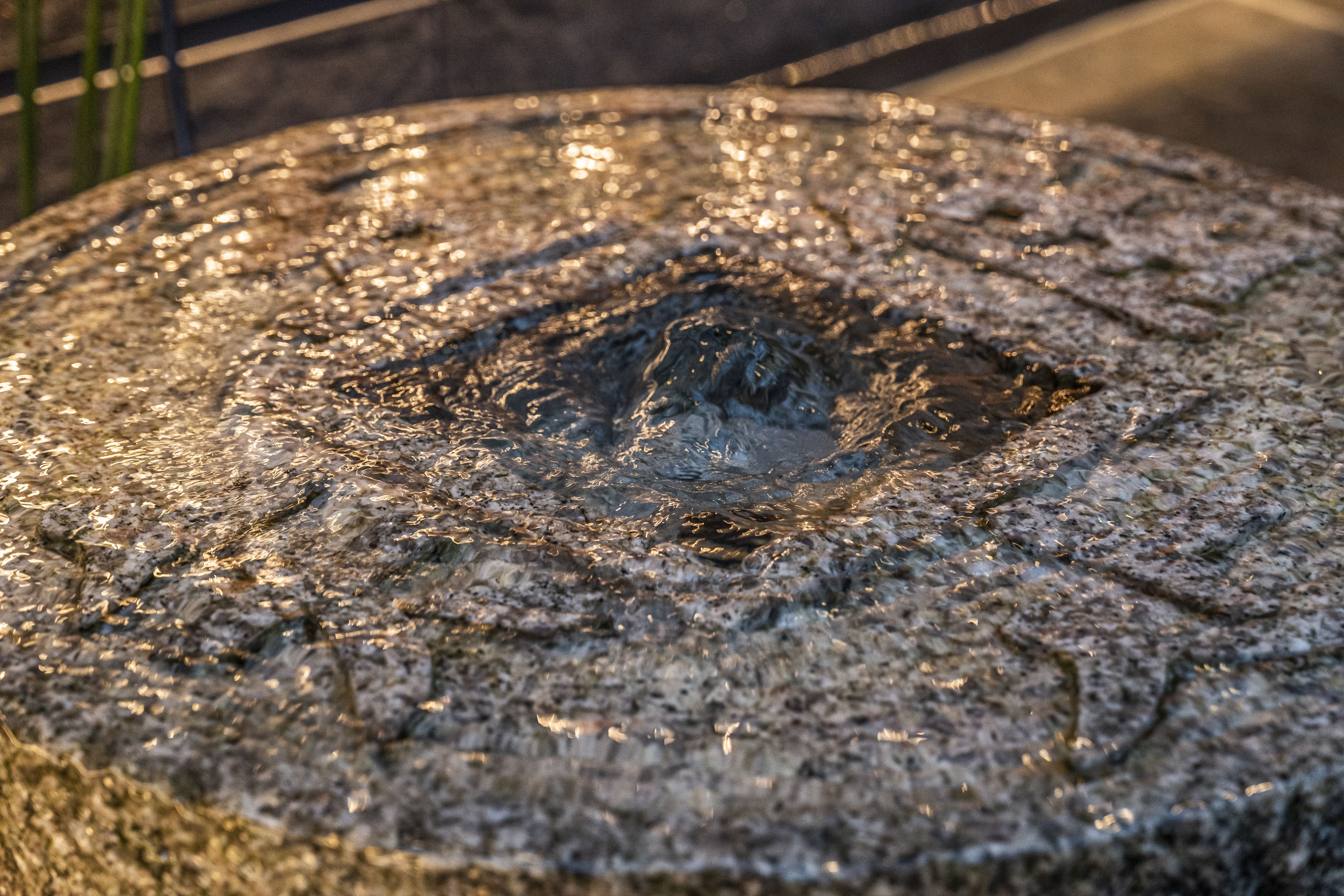 Primer plano de una superficie de piedra por donde fluye agua, creando ondas y reflejos.