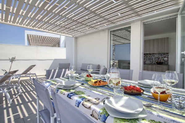An outdoor dining area with a table set for two, a grill, and a view of the sea.