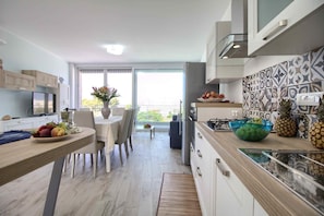 A modern kitchen with a dining area, large windows, and a view of greenery.