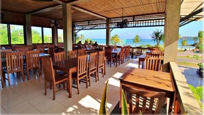 Un restaurant avec des tables et des chaises en bois, de grandes fenêtres et une vue sur l’océan.