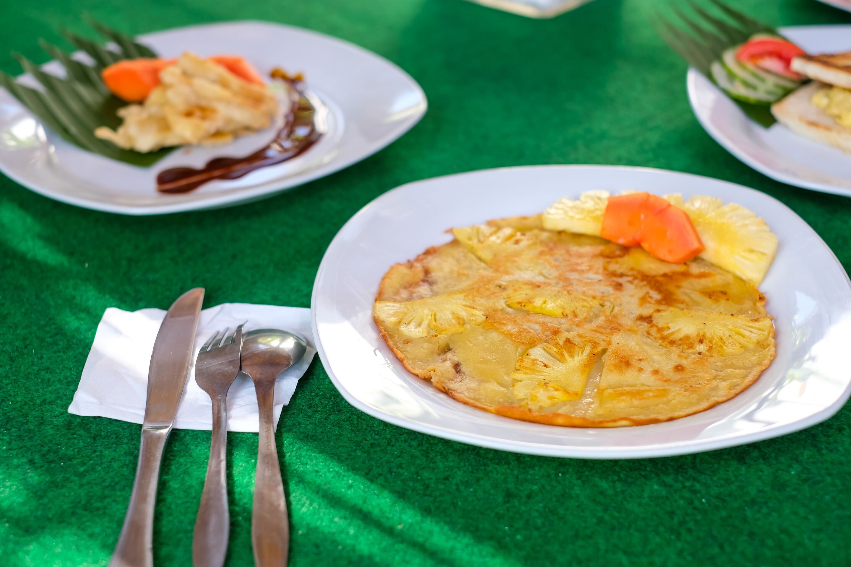 A table with plates of food, cutlery, and a green tablecloth.